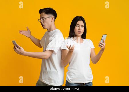 Confused asian man and woman looking at their mobile phones Stock Photo