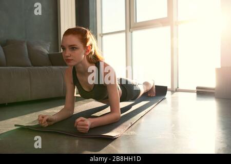 Young girl does gym exercises at home with sunrise Stock Photo