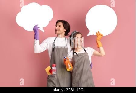 Smiling Couple Wearing Aprons And Household Gloves, Holding Empty Speech Bubbles Stock Photo