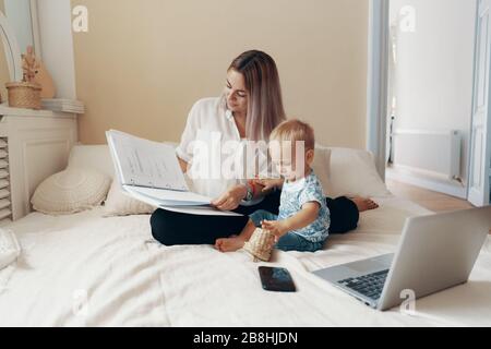 Young mother with her child working in bedroom at home. Multi-tasking, freelance and motherhood concept Stock Photo