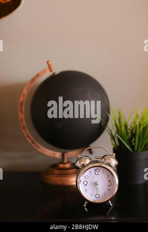 Black decorative stylish globe and clock standing on table near houseplant. Stock Photo