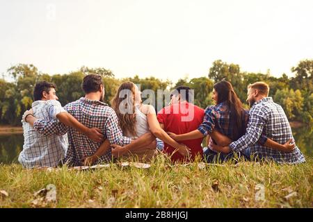 Young people sit on the grass hugging in nature in the park Stock Photo