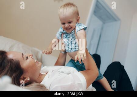 Young mother having fun laughing playing funny active games with cute child son in bedroom at home Stock Photo