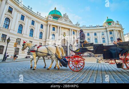 VIENNA, AUSTRIA - FEBRUARY 19, 2019: The classic horse-drawn carriage rides along the Hofburg Imperial palace in St Michael's square (Michaelerplatz), Stock Photo