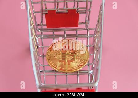 Gold coin with the image of bitcoin lies in the shopping basket. Stock Photo