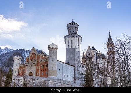 Exterior close view of the famous Neuschwanstein Castle in winter, with blue sky cloud and snow covered mountains in background, Schwangau, Bavaria, G Stock Photo