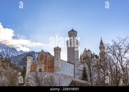 Exterior close view of the famous Neuschwanstein Castle in winter, with blue sky cloud and snow covered mountains in background, Schwangau, Bavaria, G Stock Photo