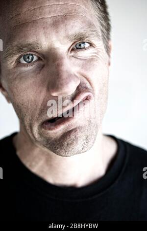 Confused man in a black T-shirt making a funny grimace looking at the camera Stock Photo
