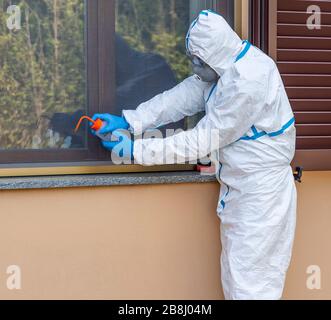 Healthcare worker with full white coverall disinfects from possible infection with Coronavirus Covid-19 using hydro alcoholic spray solution Stock Photo