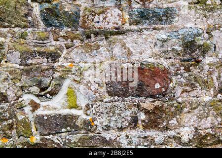 Stone wall with irregular shaped stones weather and old with small patches of moss Stock Photo