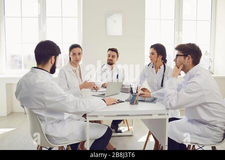 Group of practicing doctors in a meeting discuss the diagnosis of a patient standing in a clinic office. Stock Photo
