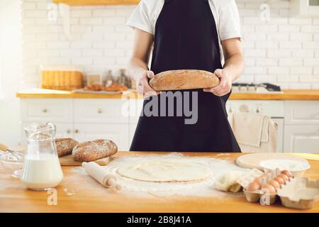 Baker man bearded man holds in his hands fresh bread standing in the kitchen. Stock Photo