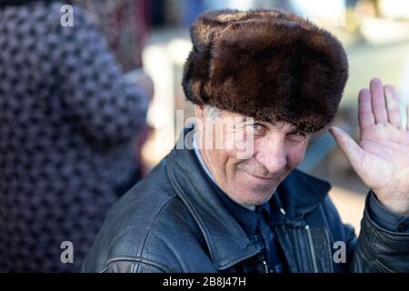 Senior local man with a fur hat waving with hand, hello, at the Street Market, Khiva, Uzbekistan Stock Photo