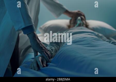 Doctor assisting a young patient at the hospital and taking pulse, she is lying on the bed and sleeping Stock Photo