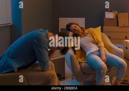 Exhausted couple relocating in their new home: they fell asleep on the armchairs after moving many cardboard boxes Stock Photo