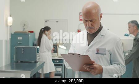 Senior scientist working in a vintage style laboratory with retro machinery, he is checking informations on a clipboard Stock Photo