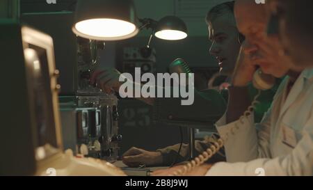 Team of scientists working in a vintage style control room, they are using computers and making phone calls Stock Photo