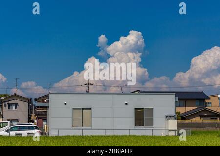 Farm building with rice paddy field in foreground, and unusual cloud formation behind, against clear blue summer sky. Kanazawa, Ishikawa prefecture, J Stock Photo