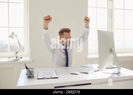 Happy blonde businessman raised his hands up working in office Stock Photo