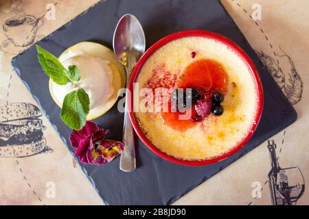 creme brulee with blueberries and raspberries topped with ice cream and decorated with violet Stock Photo