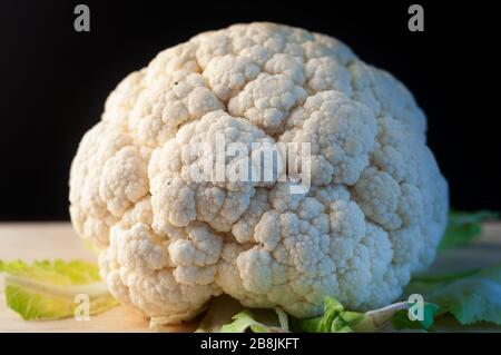 close up of a whole cauliflower on a wooden base and black background. Stock Photo