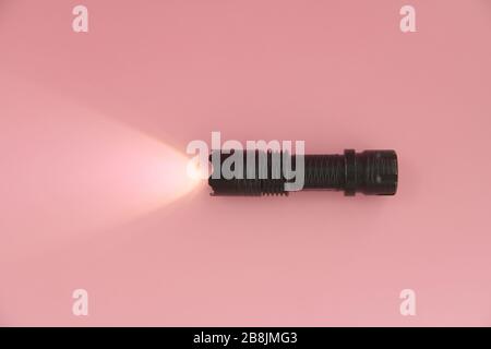 The black turned on electric manual lamp lies on a pink background. Light from a lantern on the surface. Stock Photo