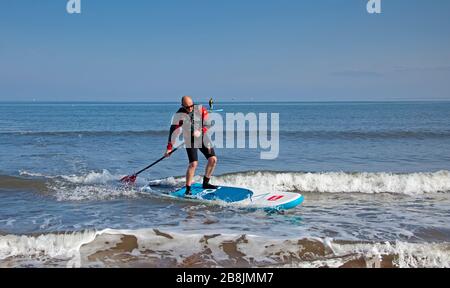 Portobello, Edinburgh, Scotland, UK. 22nd Mar 2020. Sunshine and blue skies with an early morning temperature of 2 degrees centigrade rising to 8 degrees by noon. Two stand up paddle boarders along with a variety of people out on the beach relaxing and enjoying activities to get away from the television and radio. Stock Photo