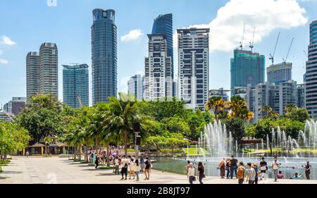 Office and residential high rise towers and fountains in Symphony Lake and tourists enjoying a day at KLCC Park Kuala Lumpur Malaysia.