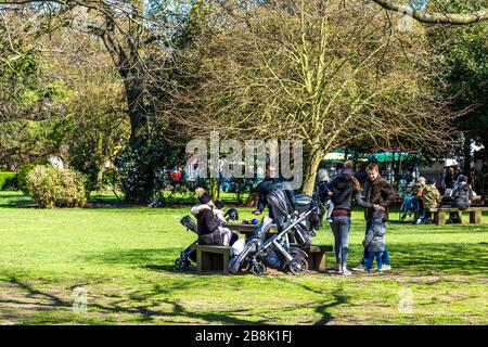 22 March 2020 - London, UK - global coronavirus pandemic, big groups of people visiting Victoria Park despite government urging people to stay at home and practice social distancing to prevent the spread of the coronavirus Covid-19, family with strollers having a picnic in the park Stock Photo