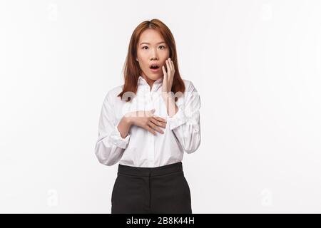 Portrait of shocked startled asian female gossiping, found out dirty little secret, open mouth and touch cheek impressed staring camera, heard rumor Stock Photo