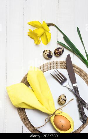 Beautiful festive Easter table setting with egg in napkin like Easter Bunny and spring flowers on white wooden table. Top view with copy space. Stock Photo