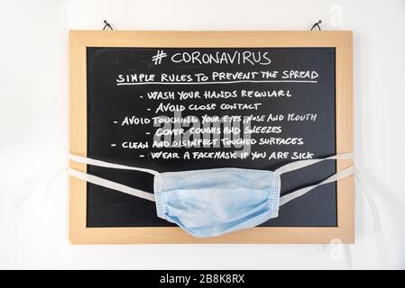 Blackboard with the rules to avoid the spread of Coronavirus with hanging safe mask. Stock Photo