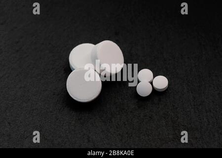 Three large white tablets and three small ones on a black background. white round pills top view. Medicare and nutritional supplements. Stock Photo