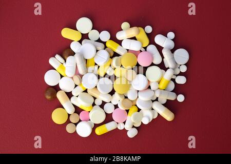 Pills of different shapes and colors on a red background top view. Many different pills during an epidemic. Medicines and nutritional supplements for Stock Photo