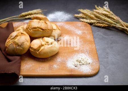 Delicious breads next to ears of wheat on a wooden board. Bakery products. Stock Photo