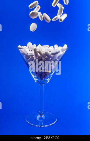 Falling white pills, tablets capsule in a martini glass on blue backround. Anti gravity concept Stock Photo