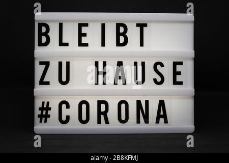 is written on an illuminated panel with black letters: Stay at home #Corona Stock Photo