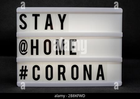 is written on an illuminated panel with black letters: Stay at home #Corona Stock Photo
