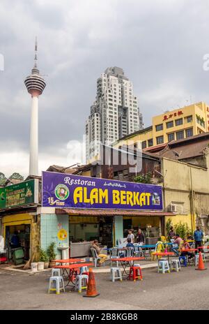 Diners eating outdoors alfresco of restaurant Alam Berkat Jalan Doraisamy street and KL Tower in background Kuala Lumpur Malaysia. Stock Photo