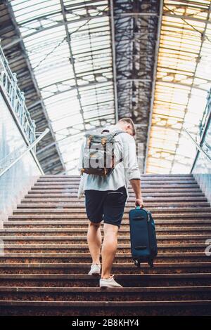 traveler man with suitcase and backpack walking up by stairs Stock Photo
