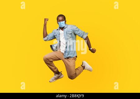 Full length portrait of joyous ecstatic man with medical mask jumping for joy or flying with raised hand, gesturing yes i did it, celebrating success. Stock Photo