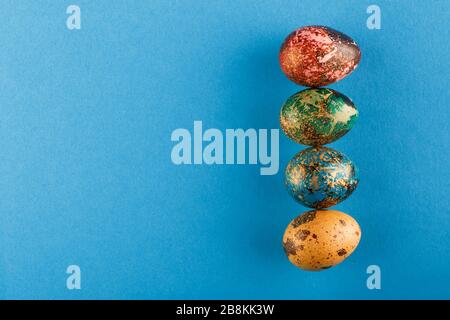 Multi-colored Easter eggs of red, green, blue, yellow color lie in a row. Painted Easter eggs on a blue background. Flat lay. Copy space Stock Photo