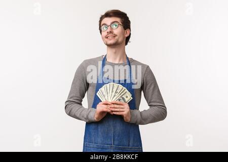 Small business, finance and career concept. Portrait of dreamy and pleased, handsome young man in apron, working at coffee shop or restaurant in apron Stock Photo