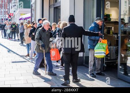 London, UK. 22nd Mar 2020. Some of the queue wear protective masks but there is still little sense that 'social distancing' is vital - Waitrose at Clapham Junction is only open to NHS workers and the over 70's for the first hour so a queue of regular customers waits outside - Anti Coronavirus (Covid 19) outbreak in London. Credit: Guy Bell/Alamy Live News Stock Photo