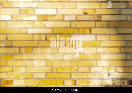 Section of an old partially weathered and polluted building wall of yellow to brownish clinker bricks with soft shadows of trees Stock Photo