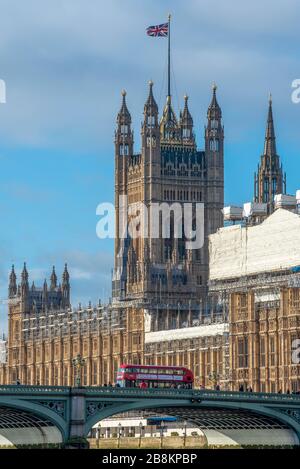A red double decker bus crosses Westminster Bridge in front of the Houses of Parliament in London, United Kingdom Stock Photo