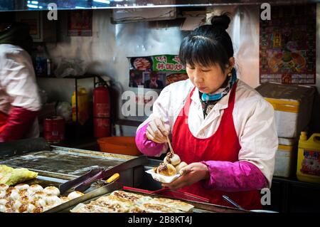 WANGFUJING NIGHT MARKET, BEIJING - DEC 25, 2013 - Female vendor serving fried pork buns at Wangfujing snack street, Beijing Stock Photo