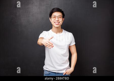 Nice to meet you. Pleasant friendly young stylish asian man in glasses and t-shirt, extend hand for handshake smiling, meeting new person, get to know Stock Photo