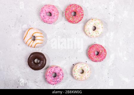 Doughnuts with multicolored glaze laid out in circle on grey concrete background. Donuts are traditional sweet pastries. Top view, flat lay, copy spac Stock Photo