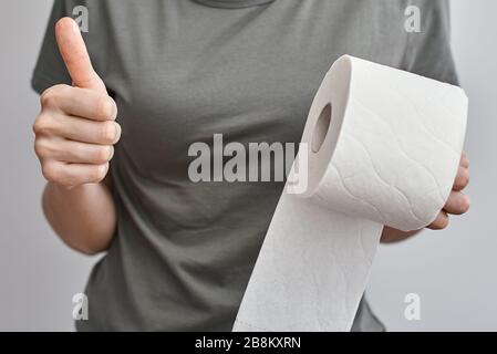 Woman hand hold toilet paper roll and show thumb up gesture, close up. Hygiene concept Stock Photo